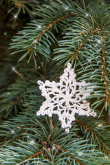 White cotton crocheted snowflake on green christmas fur tree