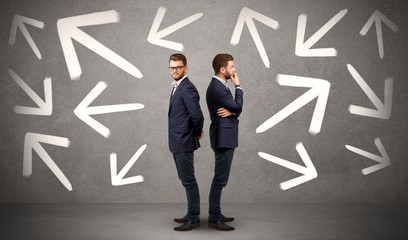 Young conflicted businessman choosing between two directions with arrows around him 