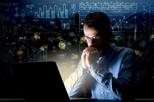 Young handsome businessman working late at night in the office with blue calculations in the background