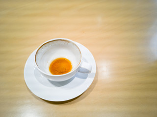 A cup of white ceramic coffee is eaten on a brown wooden table in a coffee shop.