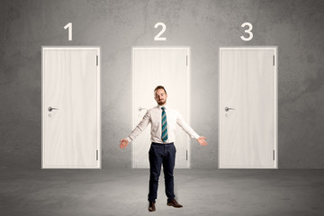 Fototapeta premium Businessman in grey room with three numbered white door behind his back 