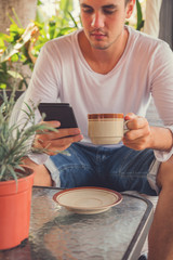 Modern man drinking coffee and using cellphone outdoors.
