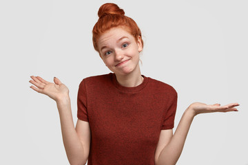 Puzzled schoolgirl cant make important decision concerning which university to enter, has clueless expression, dressed in casual burgundy t shirt, isolated over white background. Lack of confidence