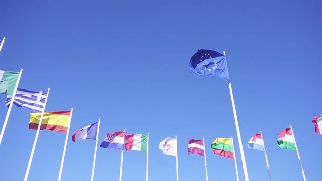 Flag of European Union with EU member flags on the background against the blue sky. Smooth slowmotion from a 120 fps original shoot
