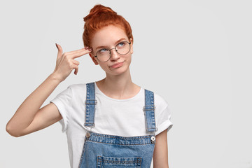 Unhappy red haired young female imitates gun shoot, makes suicide gesture, keeps two fingers on...