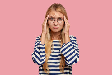 Stressful overworked busy female with displeased frustrated expression keeps hands on temples,...