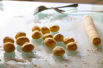 Small portions of dough are ready to form on the glass surface with flour. alongside the roll of dough.In the background is a spoon and a fork.