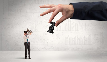 Little businessman is afraid to make the next step in his chess game with graphs, charts and...