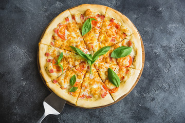 Delicious pizza with bacon, cheese, tomato and basil leaves on dark background. Flat lay, top view.