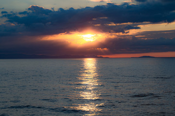 The sunset behind the clouds with the sea line with sun reflection on the water