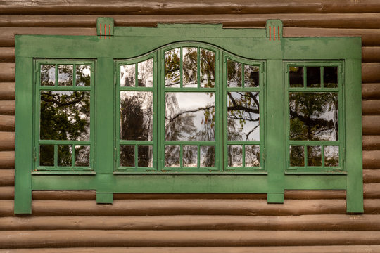 One green window with reflections on brown timber exterior building wall. Decorative traditional wooden frame.
