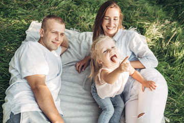 Fototapeta premium Young Adult Couple with Their Little Daughter Having Fun in the Park Outside the City, Family Weekend Picnic Concept, Three People Enjoying Summer Time