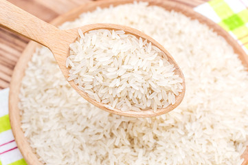 Wooden spoon with rice over wooden bowl of rice. Close up.