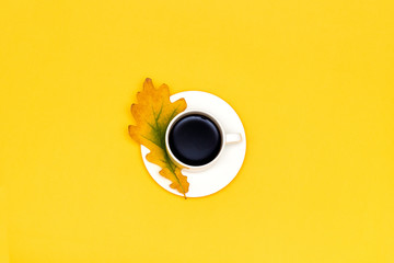 Cup of coffee and autumn oak leaf on yellow background