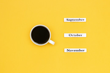 Cup of coffee and calendar November October September on yellow background