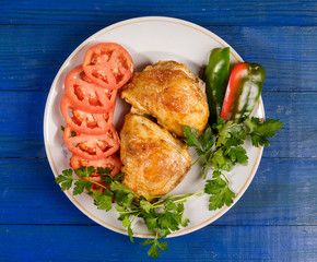 Grilled chicken with vegetables on a round plate on a blue wooden table.