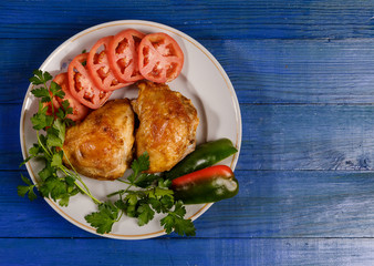 Grilled chicken with vegetables on a round plate on a blue wooden table.