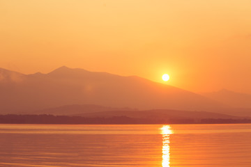 A beautiful sunrise over the lake with mountains in distance. Morning landscape in warm tones. Tatra mountains in Slovakia, Europe.