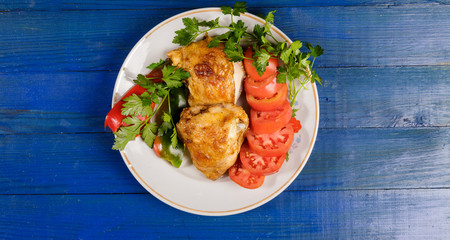 Grilled chicken with vegetables on a round plate on a blue wooden table.