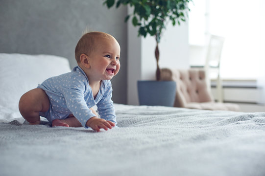 8 month old happy baby boy crawling on bed at home