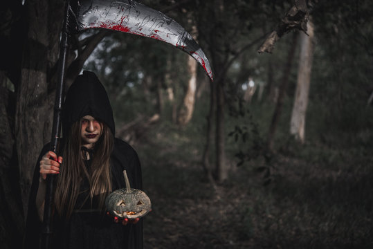 Woman ghost horror her have scythe and pumpkin on hand in forest,