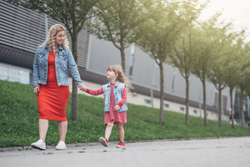 Beautiful Young Mother with Small Stylish Daughter Walks Through City Together