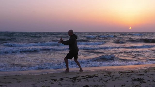 Athletic man practicing Tai Chi at sunset over the sea
