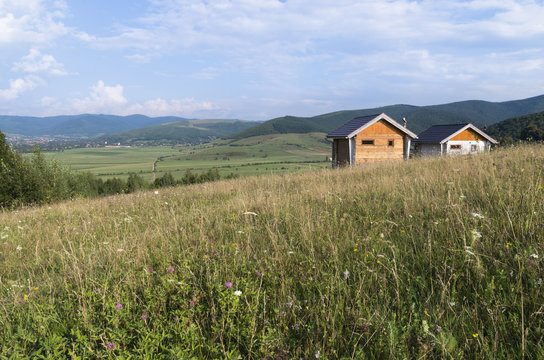 Beautiful meadows and hills with two small houses for spiritual solitude in the mountains and blue sky with clouds on sunny summer day