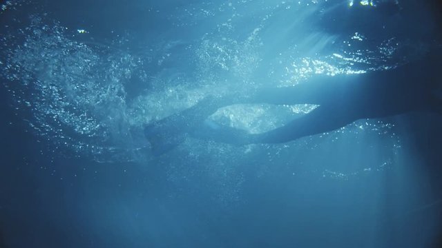 A man daving in the dark water with some sunlight s.