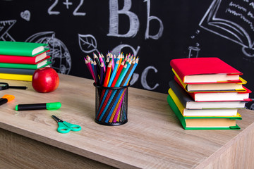 Back to school supplies. Two piles of books, felt-tip pens, magnifying glass, scissors, red apple and a chalkboard on the background