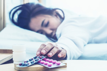 Obraz na płótnie Canvas Closeup on pills and glass of water on table and Asian women sleep sick on bed in bed room.color tone