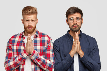Help us one more time. Two bearded friends have midserable expressions, hold hands in pray, ask for...