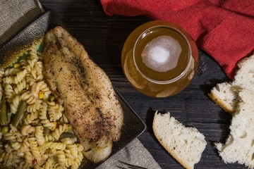 Pasta with delicious, juicy fish, beer and bread on wooden background