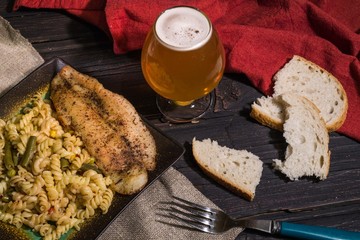 Pasta with delicious, juicy fish, beer and bread on wooden background
