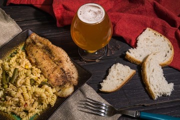 Pasta with delicious, juicy fish, beer and bread on wooden background