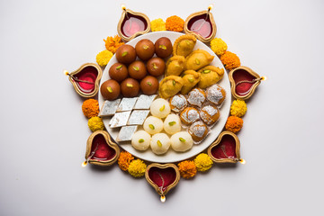 Diwali Rangoli made using Diya/oil lamp, flowers and plate full of Gulab Jamun, Rasgulla, kaju katli, morichoor / Bundi Laddu, Gujiya or Karanji 