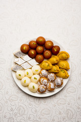 Indian sweets in a plate includes Gulab Jamun, Rasgulla, kaju katli, morichoor / Bundi Laddu, Gujiya or Karanji for diwali celebration