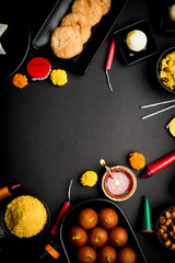 Diwali sweets and snacks arranged in a group with Diya or oil lamp, flowers and Fire Crackers or Patakhe over moody background, selective focus