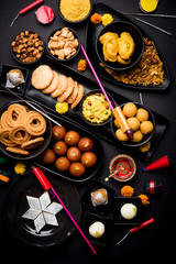 Diwali sweets and snacks arranged in a group with Diya or oil lamp, flowers and Fire Crackers or Patakhe over moody background, selective focus