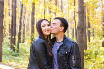 Love, relationship, family and people concept - man kissing his wife in autumn park
