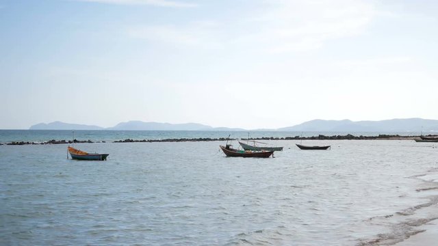 Small fishing boat parked on the shore and waves. See mountains and blue skies