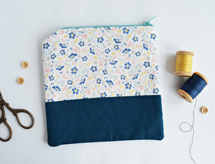 Fabric notions bag with flowers, wooden buttons, retro scissors and vintage thread spools on white