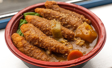 Take away chicken katsu curry with green beans and carrot in a red bowl