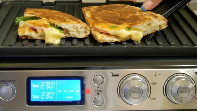 The girl removes ready-made sandwiches from the stove. Cooking bread with cheese and sausage on an electric grill. Quick hot breakfast.