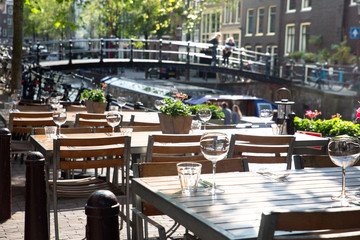 Amsterdam restaurant cafe tables set for outdoor dining with glassware and view of canal bridge in...