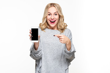 Excited happy blond woman in sweater showing blank smartphone screen and pointing on it while...