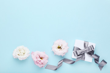 Fototapeta na wymiar Gift box with ribbon and eustoma flowers on blue background