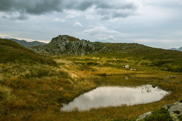 A beautiful autumn mountain landscape with a small lake. Natural scenery in Norwegian mountains. Small water pond in mountains.