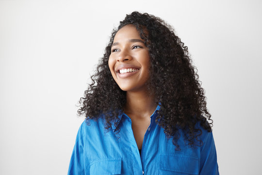 Positive human facial expressions, feeling and emotions. Picture of beautiful happy young dark skinned mixed race female with loose wavy hair looking sideways with dazzling ultra white smile