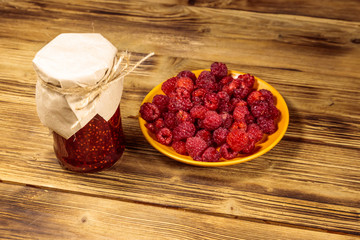 Raspberry jam in glass jar and fresh raspberries on wooden table